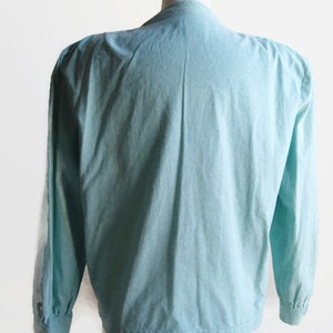 Pode incluir: Uma blusa azul claro de manga comprida com fecho de bot&otilde;es na frente e manga ligeiramente bufante.