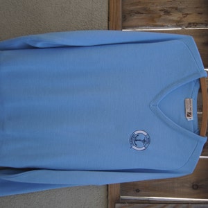 May include: A light blue v-neck sweater with a white embroidered logo that says "Royal Princess" and features an anchor inside a life preserver.
