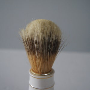 May include: A white and gold shaving brush with a full, dense brush head made of natural boar bristles.