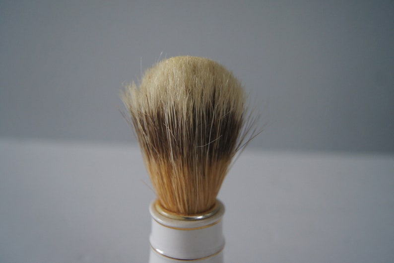 May include: A white and gold shaving brush with a full, dense brush head made of natural boar bristles.