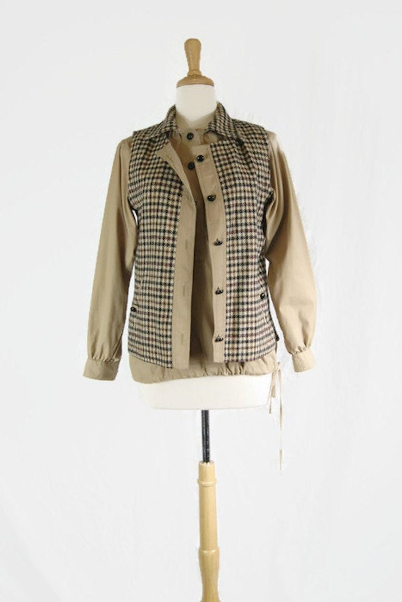 May include: A brown and black plaid vest with a button-up front and a drawstring closure. The vest is layered over a tan button-up shirt.