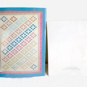 K&ouml;nnte beinhalten: Ein blaues und wei&szlig;es Quiltmuster mit rosa Rand. Das Quiltmuster ist ein traditionelles Patchwork-Design mit Quadraten in verschiedenen Farben und Gr&ouml;&szlig;en. Der Quilt tr&auml;gt den Titel "Flowers of Friendship" und ist ein Bastelprojekt von Barbara Sue. Das Urheberrecht liegt bei The Scrappers' Frolic Creative Group.