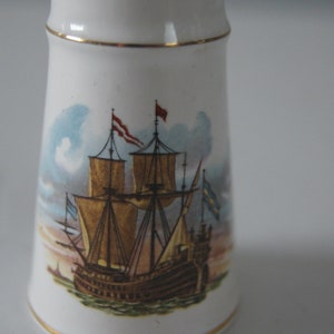 May include: White ceramic salt and pepper shaker with a gold trim. The shaker features a hand-painted image of a ship with sails and flags.
