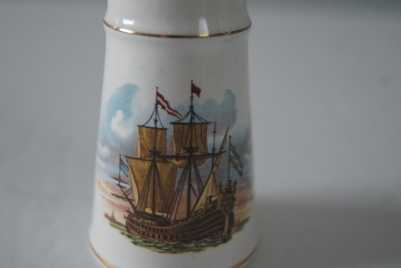 May include: White ceramic salt and pepper shaker with a gold trim. The shaker features a hand-painted image of a ship with sails and flags.