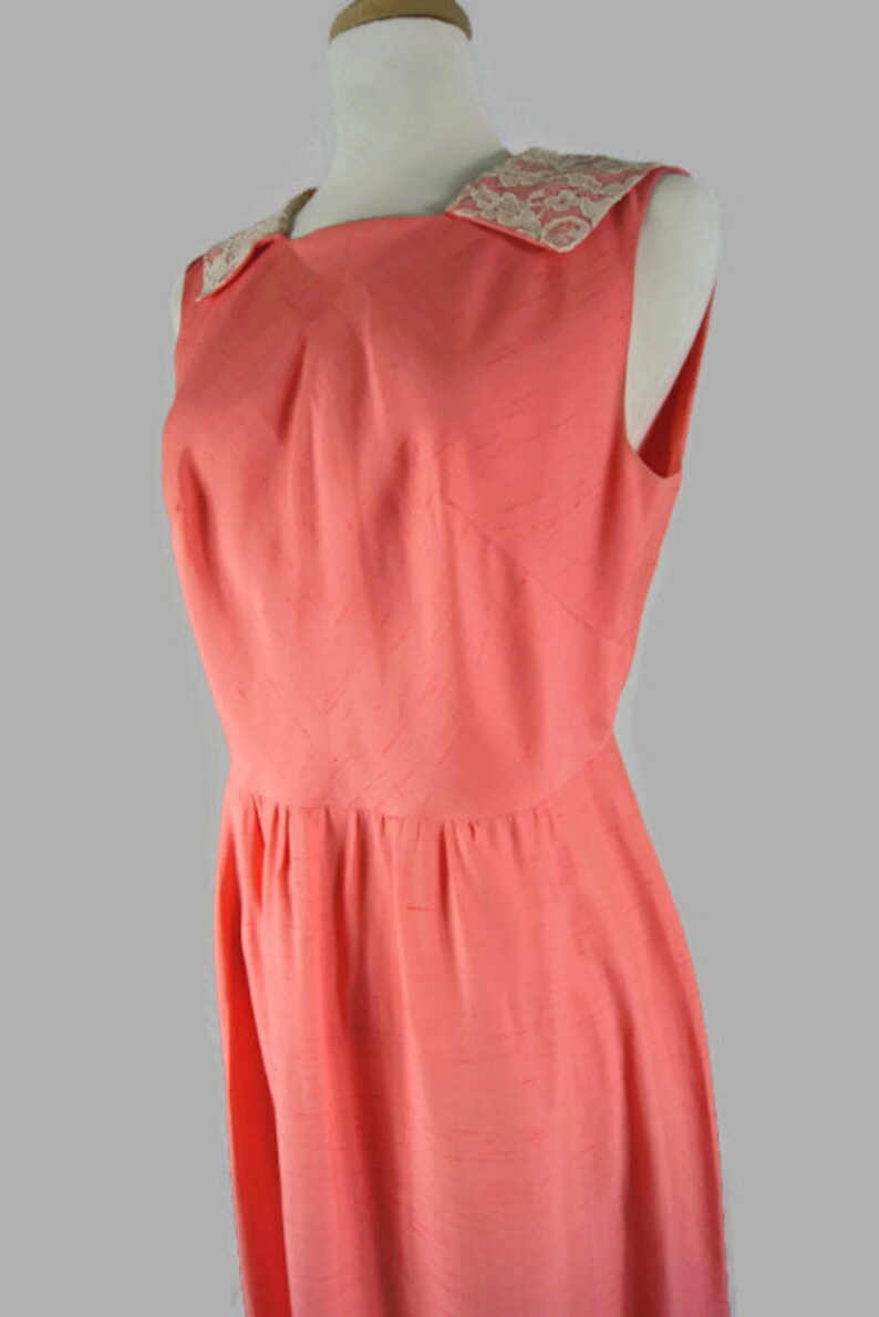 May include: A sleeveless coral pink dress with a white lace collar. The dress has a fitted bodice and a full skirt.