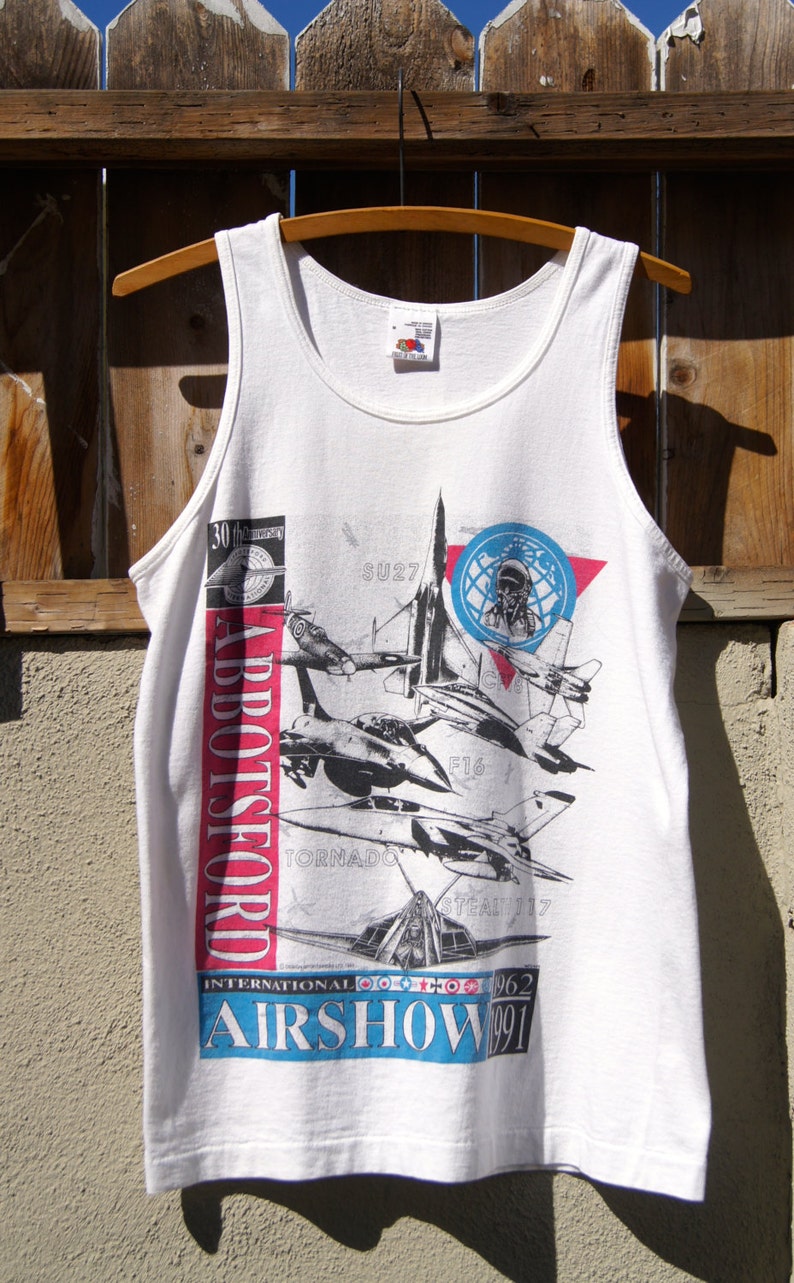 May include: White tank top with a graphic print of fighter jets and the text "Abbotsford International Airshow 1991".