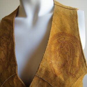 May include: A brown suede vest with a deep V-neck and decorative stitching. The vest has a unique design with two circular patterns on the front.