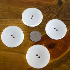 Op de afbeelding: Vier witte plastic knoppen met elk twee gaten, gerangschikt op een houten oppervlak.