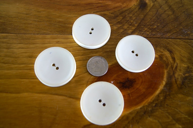 Op de afbeelding: Vier witte plastic knoppen met elk twee gaten, gerangschikt op een houten oppervlak.