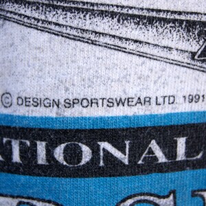 May include: A white t-shirt with a blue and black graphic of a hockey player and the text "National Hockey League". The shirt also has the text "&copy; DESIGN SPORTSWEAR LTD. 1991" printed on it.