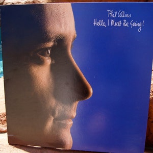 May include: A close-up of Phil Collins's face on a blue album cover. The album title is "Hello, I Must Be Going!"
