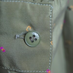 May include: A close-up of a green button with four holes on a green fabric with a white stitch around the edge.