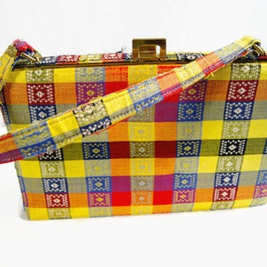 Puede incluir: Un bolso vintage con un colorido estampado a cuadros en amarillo, naranja, rojo, morado, azul y verde. El bolso tiene forma rectangular, un cierre dorado y un asa con estampado a juego.