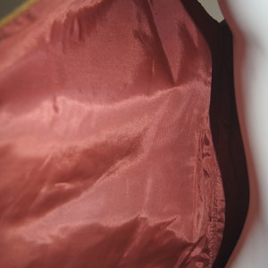 May include: A close-up of the inside of a brown leather jacket. The lining is a deep red colour and is made of a smooth, silky fabric.