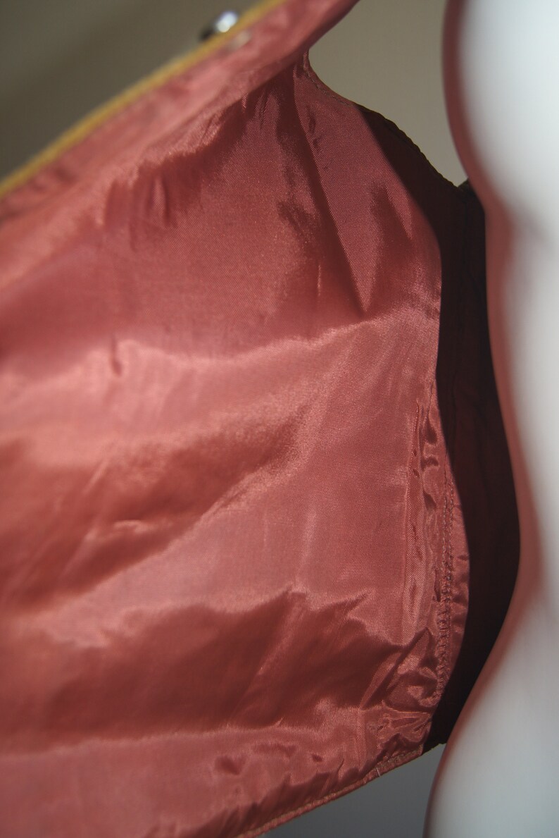 May include: A close-up of the inside of a brown leather jacket. The lining is a deep red colour and is made of a smooth, silky fabric.