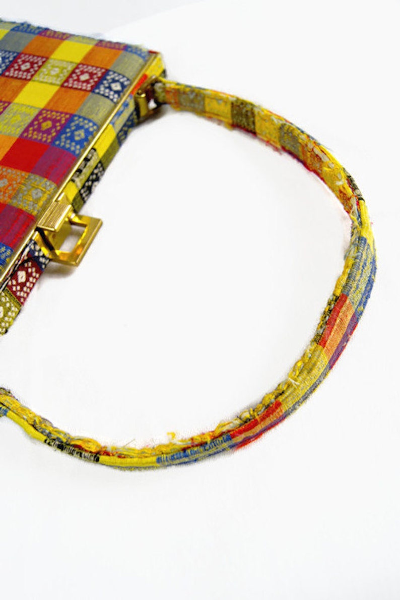 Puede incluir: Un bolso vintage con un dise&ntilde;o de patchwork colorido. El bolso presenta un cierre y accesorios de asa dorados. El asa tiene un patr&oacute;n de patchwork a juego. El cuerpo del bolso es una mezcla de cuadrados rojos, amarillos, azules y verdes.