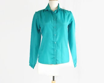 May include: A teal blue long-sleeved button-up shirt with a collared neckline. The shirt is on a white mannequin.