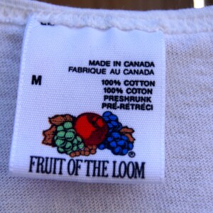 May include: White Fruit of the Loom tag with a red, green, and blue fruit design. The tag says "Made in Canada, Fabrique au Canada, 100% Cotton, 100% Coton, Preshrunk, Pre-Retreci" and "Fruit of the Loom". The tag also has a size "M" printed on it.