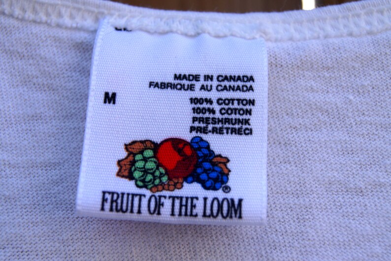 May include: White Fruit of the Loom tag with a red, green, and blue fruit design. The tag says "Made in Canada, Fabrique au Canada, 100% Cotton, 100% Coton, Preshrunk, Pre-Retreci" and "Fruit of the Loom". The tag also has a size "M" printed on it.
