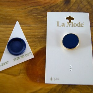 Op de afbeelding: Twee blauwe knopen met een gouden rand. De grotere knop bevindt zich op een witte kaart met de tekst "La Mode" en "&euro; 1,50". De kleinere knop bevindt zich op een witte driehoek met de tekst "Maat 30 (3/4")" en "4-3327".