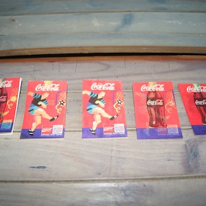 May include: Five Coca-Cola trading cards featuring a red background with a soccer player and a Coca-Cola bottle. The cards have the text "Coca-Cola" printed on them.