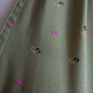 May include: Close-up of a green fabric with a repeating pattern of small, geometric shapes in yellow, pink, and black.