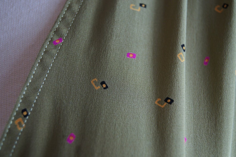 May include: Close-up of a green fabric with a repeating pattern of small, geometric shapes in yellow, pink, and black.