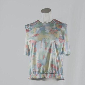 May include: A short-sleeved top with a floral pattern in pastel colors of pink, blue, yellow, and green. The top has a gathered elastic waist and a round neckline. The shoulders have a slight puff detail. The fabric appears to be lightweight.