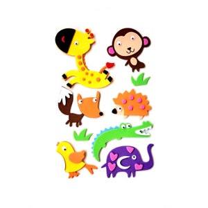 Peut inclure: Une collection de découpes d'animaux en mousse colorée, comprenant une girafe, un singe, un renard, un hérisson, un crocodile, un oiseau et un éléphant. La girafe est jaune avec des taches marron, et l'éléphant est violet avec des cœurs roses. Fond blanc.