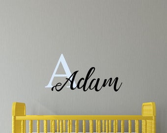 Könnte beinhalten: Ein gelbes Babybett mit einer weißen Matratze und einem schwarzen Vinyl-Aufkleber an der Wand, auf dem "A Adam" steht.