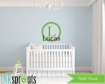 Könnte beinhalten: Ein weißes Babybett mit einem personalisierten Wandaufkleber in Grün und Braun mit dem Buchstaben L und dem Namen Lucas.