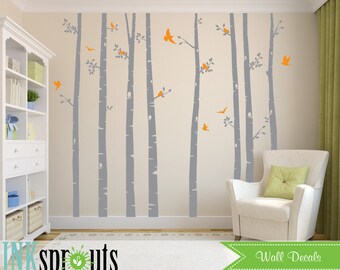 Könnte beinhalten: Graue Birkenbaum-Wandaufkleber mit orangefarbenen Vögeln. Die Aufkleber sind in einer Waldszene auf einer hellbeigen Wand angeordnet. Der Text "Wall Decals" ist in der rechten unteren Ecke des Bildes sichtbar.