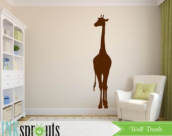 Könnte beinhalten: Braune Silhouette eines Giraffen-Wandaufklebers an einer weißen Wand in einem Raum mit einem weißen Bücherregal und einem weißen Sessel mit einem grünen Kissen.