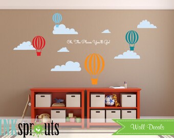 Könnte beinhalten: Wandaufkleber mit bunten Heißluftballons und weißen Wolken auf einer braunen Wand. Der Satz "Oh, The Places You'll Go!" ist kursiv geschrieben. Darunter befindet sich ein rotes Regal mit weißen Boxen.
