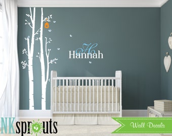 Könnte beinhalten: Wandaufkleber für das Kinderzimmer mit einem Design aus weißen Birken, einem orangefarbenen Vogelhaus und kleinen Vögeln. Der Name "Hannah" wird in weißer und blauer Schrift über einem weißen Kinderbett angezeigt. Die Worte "Wall Decals" stehen auf einem grünen Banner.