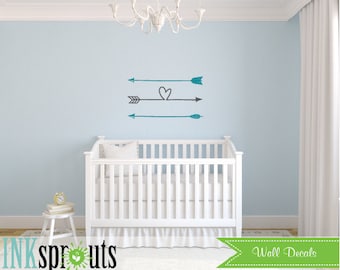 Könnte beinhalten: Wandaufkleber mit drei Pfeildesigns in Türkis und Grau, mit Herzakzent. Die Aufkleber werden an einer hellblauen Wand über einem weißen Kinderbett gezeigt. Das Bild enthält den Text "INK sprouts" und "Wall Decals".