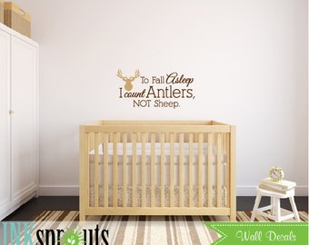 Könnte beinhalten: Eine braune Hirschkopf-Silhouette mit dem Text "To Fall Asleep I count Antlers, NOT Sheep." an einer weißen Wand über einem Holzbett in einem Kinderzimmer.