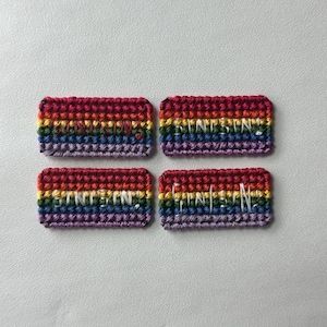 May include: Four rectangular, crocheted patches with a rainbow gradient of colors. Each patch has the word "STINTIN" embroidered in white thread. The patches are arranged in a square on a light gray surface.