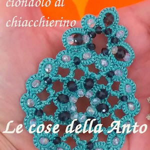Może przedstawiać: Turkusowy kolczyk lub wisiorek wykonany na szydełku z czarnymi i tęczowymi koralikami. Na zdjęciu widoczny jest tekst "Schema di orecchino o ciondolo al chiacchierino" i "Le cose della Anto".