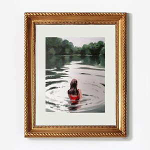 May include: A framed painting of a woman in a red swimsuit swimming in a lake. The water is calm and the woman is looking out at the trees on the other side of the lake.