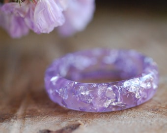 May include: A purple resin ring with silver flakes embedded in the resin. The ring is on a wooden surface.
