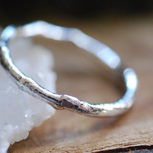 Puede incluir: Un anillo de plata con un diseño texturizado de aspecto orgánico. El anillo está hecho de una banda delgada de metal y tiene una superficie rugosa y desigual.