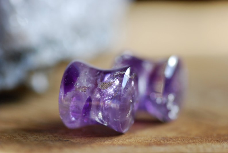 Puede incluir: Dos tapones de amatista, uno morado y otro morado claro, con un ligero brillo iridiscente.