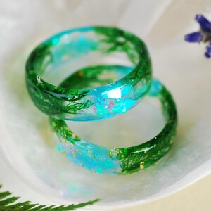 Op de afbeelding: Twee groene en blauwe harsringen met ingebed groen gebladerte en gouden glitter. De ringen zijn op elkaar gestapeld.