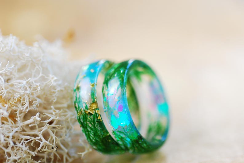 Op de afbeelding: Twee harsringen met een groen, blauw en gouden ontwerp. De ringen zijn op elkaar gestapeld.
