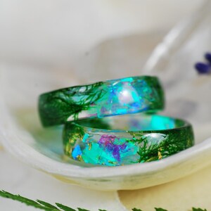 Op de afbeelding: Twee groene harsringen met ingebedde iriserende glitter en gedroogde botanische elementen. De ringen zijn op elkaar gestapeld.