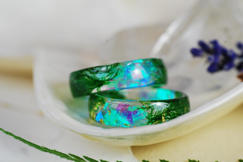 Op de afbeelding: Twee groene harsringen met ingebedde iriserende glitter en gedroogde botanische elementen. De ringen zijn op elkaar gestapeld.