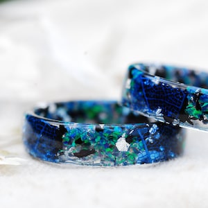 May include: Two resin rings with blue, green and silver glitter embedded in the resin. The rings are stacked on top of each other.