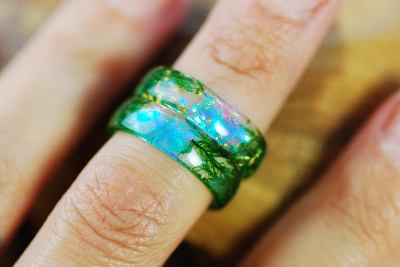 Op de afbeelding: Een paar groene harsringen met iriserende blauwe en roze accenten. De ringen zijn op elkaar gestapeld en hebben een glinsterende afwerking.