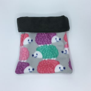 May include: A gray fleece pet bed with a dark green folded over top. The bed is patterned with colorful cartoon hedgehogs in pink, purple, red, and green. The hedgehogs have white faces and are smiling.
